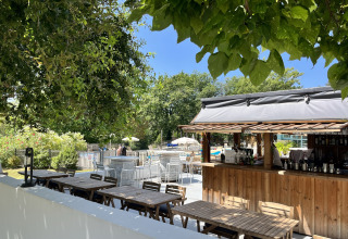 Area caffè all'aperto con tavoli in legno, bar e piscina presso Whaka Lodge glamping nel sud della Francia.