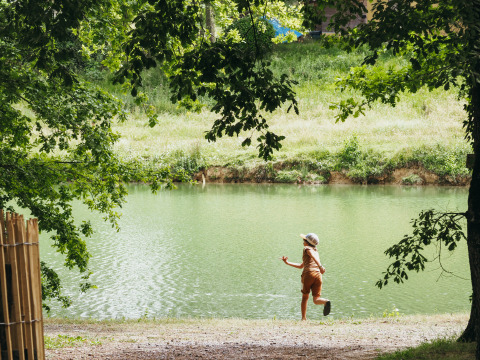 Enfant jouant près du lac sous les arbres au Whaka Lodge, camp nature et glamping dans le sud de la France.