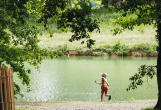 Bambino che gioca vicino al lago sotto gli alberi a Whaka Lodge, glamping immerso nella natura nel sud della Francia.