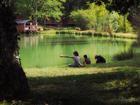 Kinder angeln am See beim Whaka Lodge Glamping in Südfrankreich, umgeben von Natur und Holzhütten.