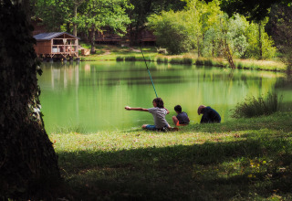 Niños pescando junto al lago en Whaka Lodge glamping en el sur de Francia, rodeados de cabañas y naturaleza.