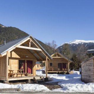 Alojamiento glamping en Huttopia Winter Chalets – Bourg St Maurice con cabañas de madera y montañas nevadas.