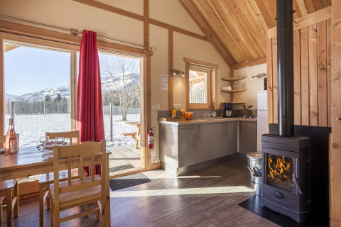 Intérieur d’un chalet glamping chaleureux avec poêle à bois et vue sur les montagnes enneigées chez Huttopia Winter Chalets.