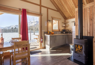 Indendørs glamping hytte med træinteriør, brændeovn og udsigt til snedækkede bjerge ved Huttopia Winter Chalets.