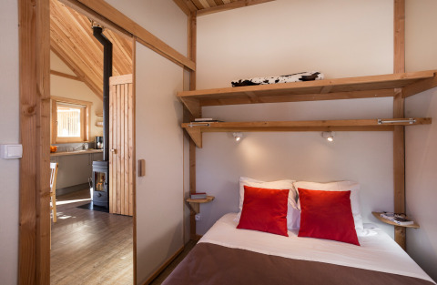 Intérieur de Huttopia Winter Chalets – Bourg St Maurice avec chambre confortable et cuisine en bois au fond.