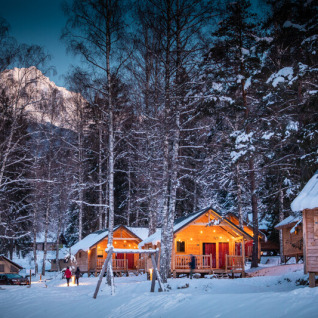 Chalet glamping invernali a Huttopia Vanoise, Bozel, Savoie, immersi tra alberi innevati e montagne.