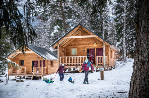 Winter glamping at Huttopia Winter Chalets in Bozel, Savoie, with families enjoying snow by cozy wooden cabins.