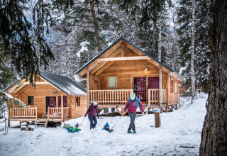 Glamping de invierno en Huttopia Winter Chalets en Bozel, Savoie, familias disfrutan la nieve frente a cabañas.