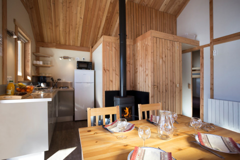 Interior of a cozy wooden chalet at Huttopia Winter Chalets, Camping Huttopia Vanoise, Bozel with table and stove.