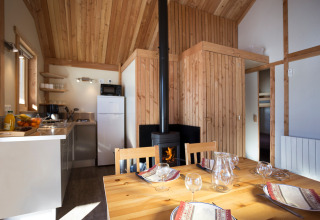 Interno di uno chalet in legno accogliente presso Huttopia Winter Chalets, Camping Huttopia Vanoise, Bozel con tavolo e stufa.