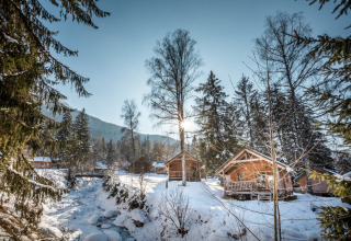 Glamping invernal en Huttopia Vanoise con cabañas de madera, árboles nevados y arroyo cristalino.