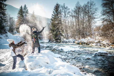 Deux personnes s’amusent dans la neige près de la rivière aux Chalets d’Hiver Huttopia Vanoise à Bozel, Savoie.