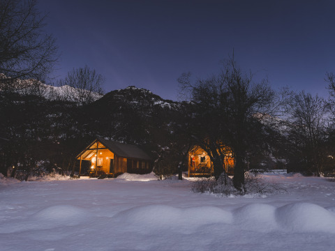 Zwei beleuchtete Hütten im Schnee bei Nacht in Huttopia Winter Chalets, Vallouise, französische Alpen.