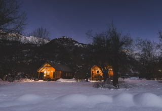 To oplyste trächytter i sneklædt landskab ved nat i Huttopia Winter Chalets, Vallouise, franske Alper.