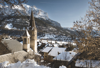 Vista invernal de Vallouise con tejados nevados y montañas cerca de Huttopia Winter Chalets, Alpes franceses.