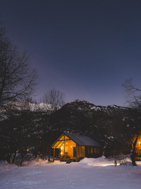 Cabaña iluminada de madera en paisaje nevado en Huttopia Winter Chalets, Vallouise, Alpes franceses.