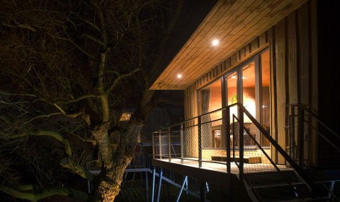 Baumhaus-Glamping-Unterkunft am Elbinselhof Krautstrand, nachts gemütlich beleuchtet.