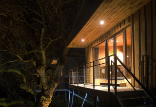 Alojamiento glamping en casa de árbol en Elbinselhof Krautstrand, iluminado cálidamente por la noche.