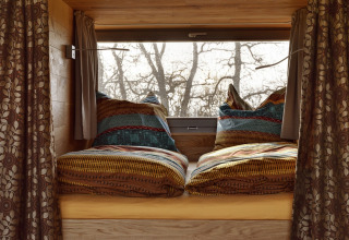 Lit de glamping douillet avec une literie colorée dans les Boomhutten d’Elbinselhof Krautstrand.