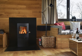 Zona lounge glamping moderna a Elbinselhof Krautstrand con stufa a legna e accogliente angolo in legno.