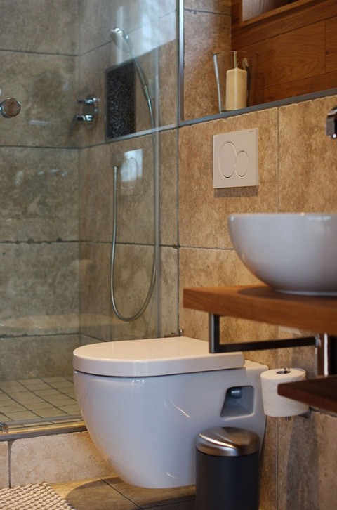 Modern bathroom with wall-mounted toilet, vessel sink, and shower in glamping accommodation, wood accents.