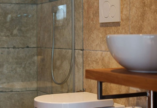 Baño moderno con inodoro suspendido, lavabo estilo bol y ducha en alojamiento glamping con detalles en madera.