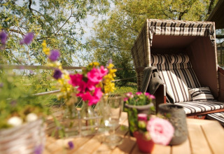 Buiten ontspanningsruimte met bloemen, bomen en een gestreepte stoel bij Elbinselhof Krautstrand glamping.