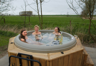 Three women relax in a hot tub with wine, enjoying the nature at Elbinselhof Krautstrand, Lower Saxony.