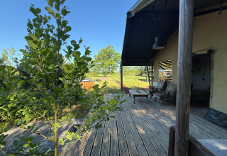 Blick von der Holzterrasse der Koakelbonts Lovenest Safaritent Gelderland mit Sitzbereich und Natur.