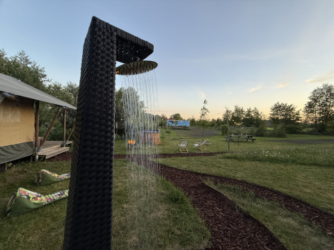 Douche extérieure près de la tente safari Koakelbonts Lovenest à Gelderland, avec pelouse et espaces détente.