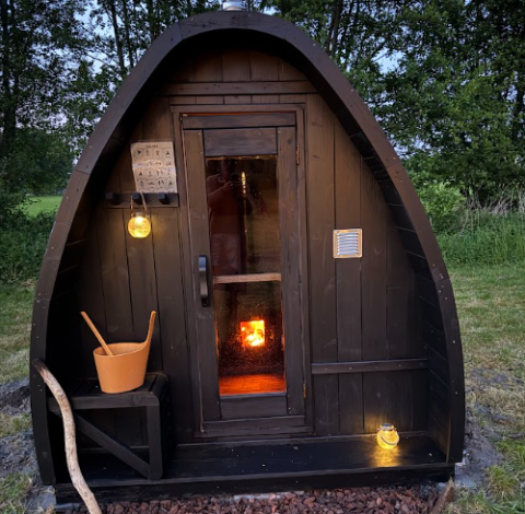 Cabane en bois chaleureuse avec poêle au Koakelbonts Lovenest - Safaritent Gelderland au crépuscule.