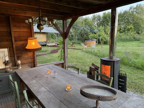 Outdoor dining area with rustic wooden table, wood stove, and glamping safari tent at Koakelbonts Lovenest.