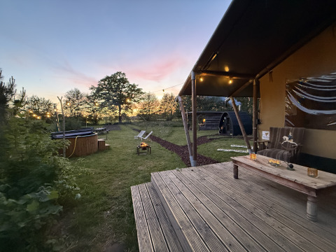 Atardecer en Koakelbonts Lovenest - Safaritent Gelderland con terraza, fogata, jacuzzi y luces cálidas.