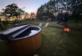 Glamping-Platz bei Sonnenuntergang mit Hot Tub, Feuerstelle, Liegestühlen und Safarizelt in Gelderland.