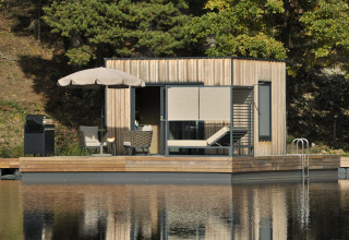Casa flotante en Nature Resort Natterer See, Tirol, con terraza de madera y entorno natural junto al lago.