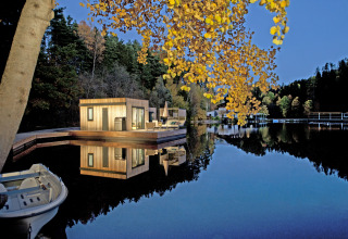Maisons flottantes du Nature Resort Natterer See - Floating Homes Tirol, entourées de forêt et eau calme au crépuscule.