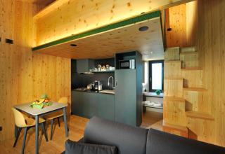 Alojamiento glamping moderno Tiny House Tirol de madera con cocina, mesa y escaleras en Nature Resort Natterer See.
