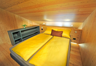Tiny House Tirol au Nature Resort Natterer See avec literie jaune et plafond en bois incliné dans un intérieur cosy.