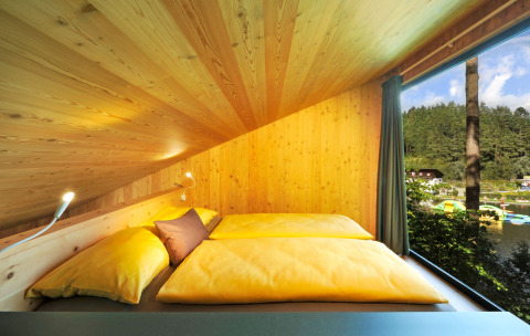 Tiny House Tirol Glamping-Unterkunft im Nature Resort Natterer See mit gemütlichem Bett und Seeblick.