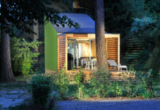 Oplyst glamping-hytte ved Nature Resort Natterer See - Tiny House Tirol omgivet af grøn skov om aftenen.