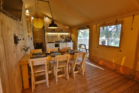 Binnenaanzicht van een luxe safaritent bij Frei wie der Wind met eettafel, houten stoelen en keuken.