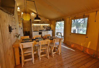 Vista interior de una tienda safari de lujo en Frei wie der Wind con mesa de comedor y cocina equipada.