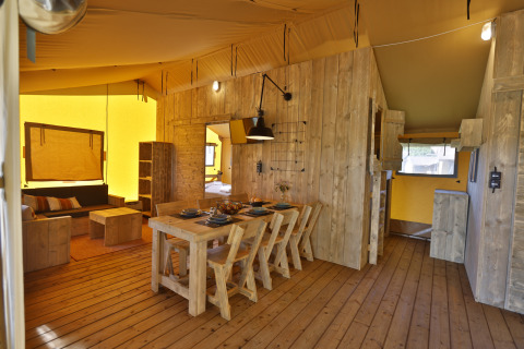 Interieur van een luxe safaritent met houten meubels, eettafel en gezellige zithoek aan de Oostzee in Duitsland.