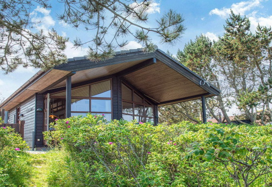 Casa vacanze moderna per 4 persone a Glesborg, circondata da verde e alberi sotto un cielo azzurro.