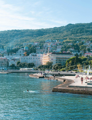 Kustplaats met huizen op de heuvel en mensen die zonnen aan het water in Mali Lošinj, Kroatië.