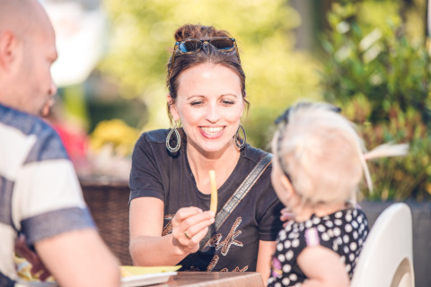 Vrouw glimlacht en biedt een frietje aan een jong kind aan tijdens een zonnige dag in vakantiepark Ackersate.