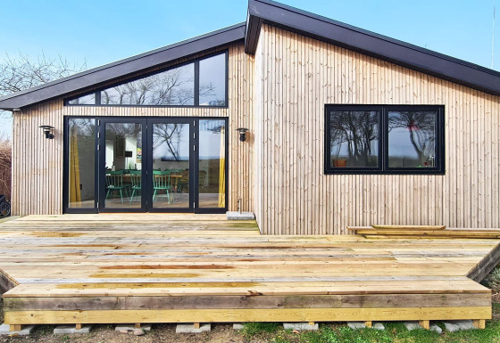 Moderne lodge med træfacade og stor terrasse i Sydals, set fra forsiden, ideel til ferieophold.