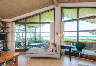 Bright living room in a holiday home in Glesborg, Denmark, with large windows overlooking the sea.