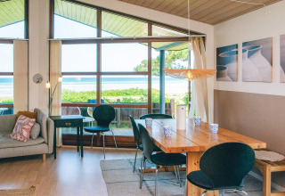 Bright living and dining area in a holiday home in Glesborg, Denmark, with large windows and sea view.