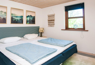 Schlafzimmer mit Doppelbett, Naturbildern und Fenster in einem Ferienhaus in Glesborg, Dänemark.